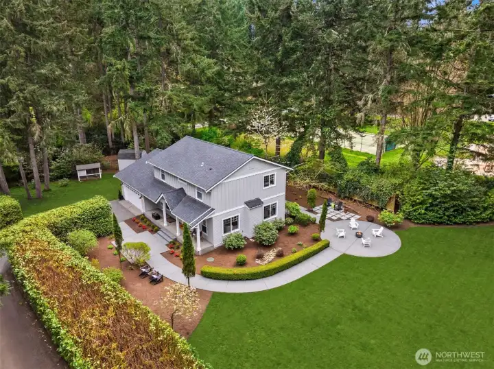 Aerial perspective reveals the full composition—gracefully sited on a generous, level parcel, with curated outdoor living spaces and a natural perimeter of mature trees offering privacy and presence.