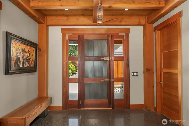 Interior foyer showcases the inside of the one-of-a-kind, 4-inch-thick custom 8’x8’ front entry door built from old-growth cedar and heavy metal. Accented by pristine, clear vertical grain fir trim, custom light fixtures, and polished concrete floors.