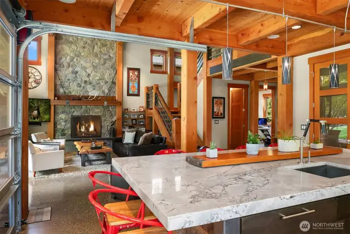 Perfect architectural synergy. This view from the kitchen island highlights the home's open-concept flow, looking past the timber frame supports directly into the great room with its towering natural stone fireplace.
