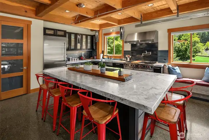 Designed for effortless hosting, the expansive kitchen layout showcases soaring timber beams, premium integrated appliances, and a custom built-in window bench perfect for guests to gather lounge-style near the chef.