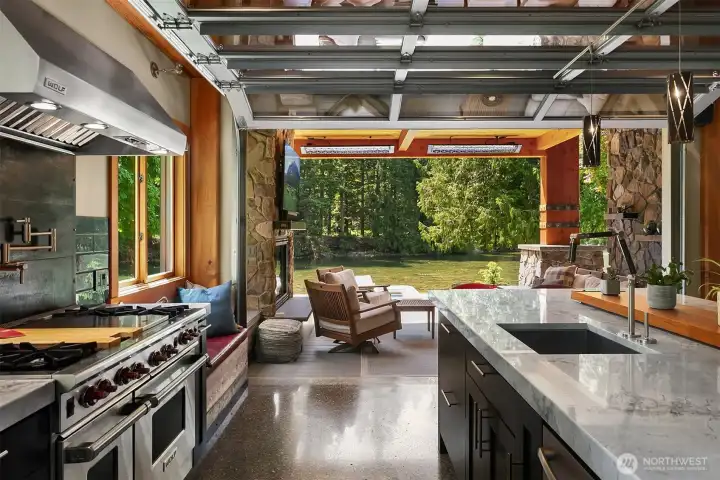 Sweeping dual-aspect views from the kitchen island sink. Look out through the glass garage door or the adjacent multi-slide glass wall to capture uninterrupted vistas of the lawn, towering evergreens, and the river.