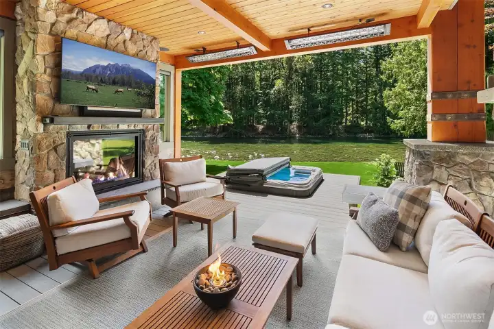 The ultimate year-round outdoor living room. This covered timber patio features a floor-to-ceiling stone fireplace, flush-mounted Infratech heaters, an integrated media center, and a pristine swim spa/hot tub right on the river's edge.