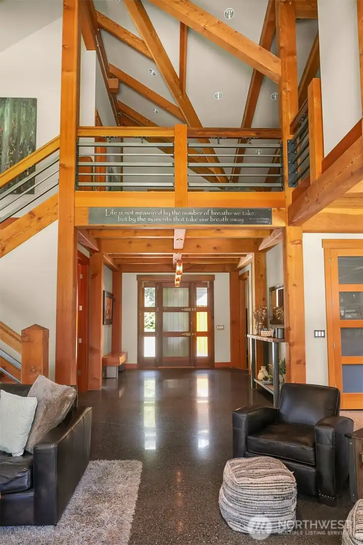 A breathtaking first impression. The grand foyer showcases soaring multi-story timber frame construction, a custom statement staircase, radiant-heated concrete floors, and direct sightlines through the home.