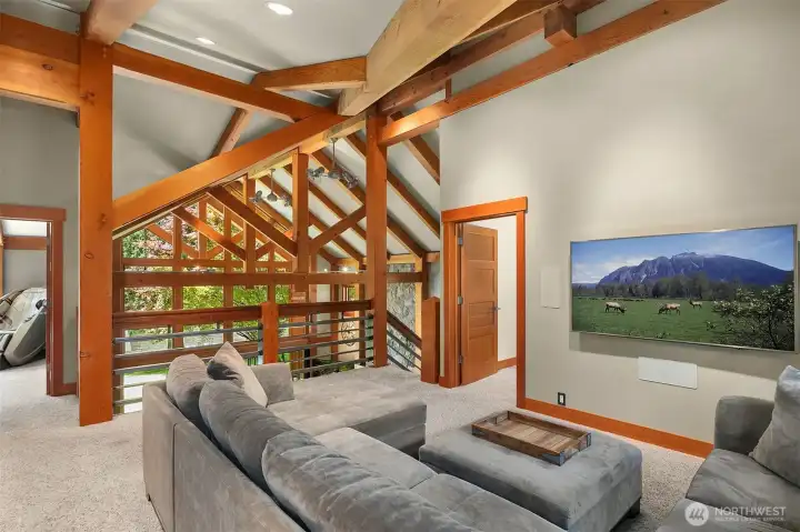 The spacious upper-level loft serves as a versatile media room or second family lounge. Dramatic timber trusses and custom iron railings offer an open architectural perspective overlooking the great room below.
