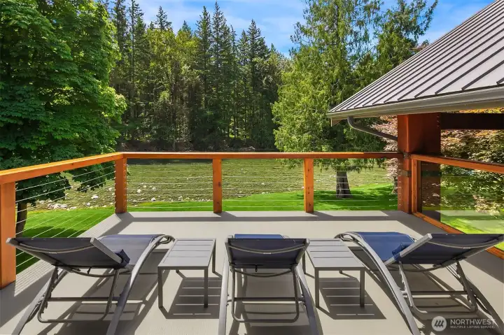 The private primary suite deck offers a peaceful morning escape. Outfitted with high-end cable railings to ensure completely unobstructed, sweeping vistas of the flowing river and the evergreen forest beyond.