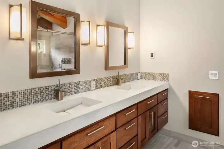 The spa-inspired primary en-suite bathroom displays a sleek, modern double vanity with clean-lined under-mount sinks, premium hardware, a mosaic tile backsplash, and fine wood cabinetry.