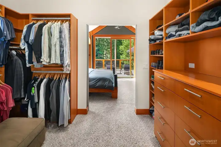 A meticulously designed primary walk-in closet featuring extensive custom built-in shelving, drawers, and wardrobe hanging systems, complete with a seamless view extending out toward the river.