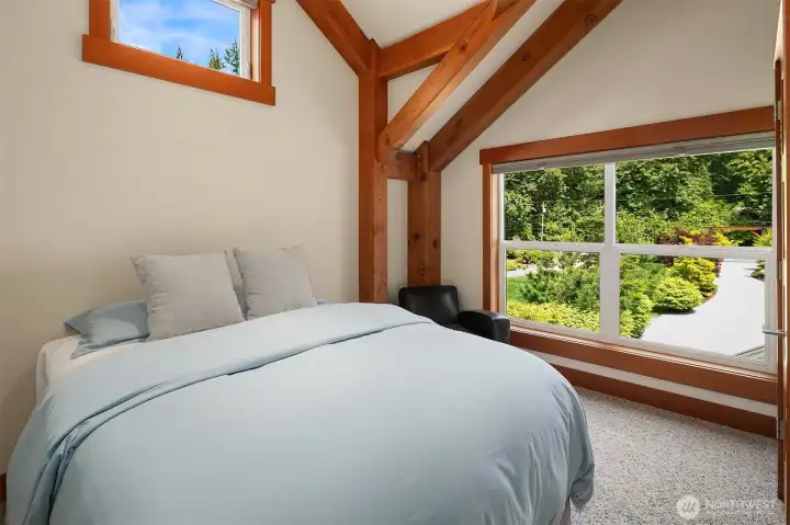 The serene main-house guest suite offers a private retreat for visitors, highlighted by signature soaring vaulted ceilings, exposed timber frame details, and a massive window framing lush garden views.