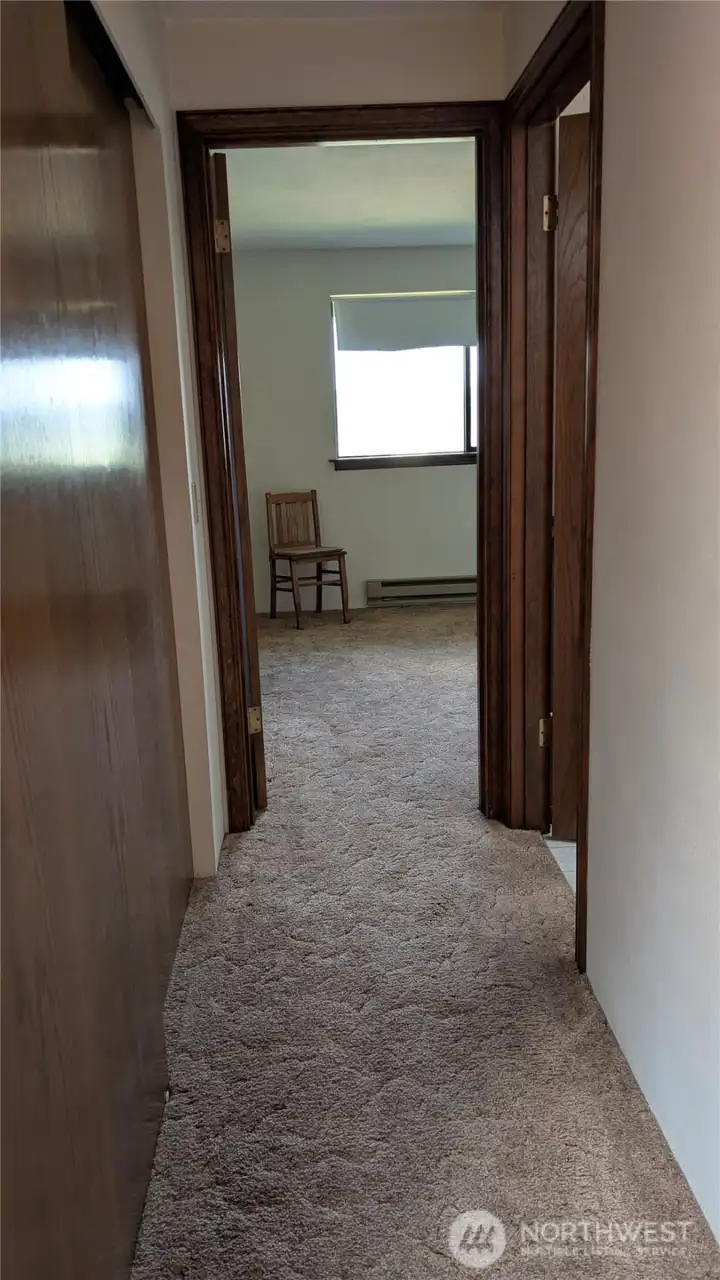 Hallway to 2nd bedroom. On the left is shelving and on the right is a full bathroom.