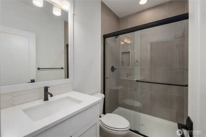 Main-Level Guest Bathroom:  This well-appointed bath features a wide quartz-topped vanity, soft neutral tilework, and a frameless glass shower enclosure accented with matte black hardware. Its thoughtful layout supports comfort and convenience for guests or main-level living. With Gooden Hollow’s Bothell location in the Canyon Park corridor, this space benefits from close proximity to parks, everyday amenities, and major commuter routes. Clean lines and modern fixtures bring a polished, cohesive feel to this main-floor bath.    These photos are from Lot 5 at Gooden Hollow, which is the same floorplan, but a different home than listed here. However, other homes in the community will have changes, so all photos, renderings, site maps, and floorplans are for visualization purposes only. Plans, colors, building orientation, finishes, home outlook, and other details can and WILL vary.