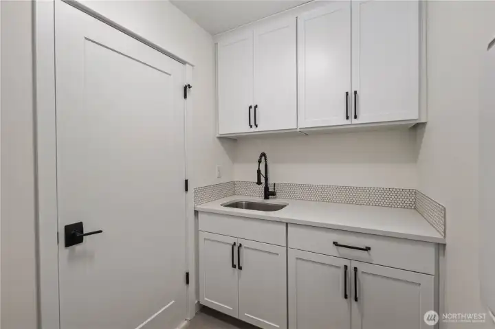 Laundry Room (Sink + Cabinetry Wall):  A secondary laundry workspace features expansive countertop space, deep utility sink, and full-height cabinetry for storing essentials. This thoughtful layout supports multitasking—folding, soaking, sorting—while keeping the rest of the home clutter-free. Positioned in Bothell’s Canyon Park neighborhood, it brings a practical rhythm to daily living near local shops, trails, and commuter routes. The stylish tile backsplash adds subtle texture and elevates the room with a polished, modern touch.    These photos are from Lot 5 at Gooden Hollow, which is the same floorplan, but a different home than listed here. However, other homes in the community will have changes, so all photos, renderings, site maps, and floorplans are for visualization purposes only. Plans, colors, building orientation, finishes, home outlook, and other details can and WILL vary.