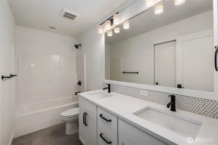 Upper-Level Full Bathroom:  This well-appointed full bath blends modern styling with everyday functionality, featuring a long quartz-topped dual-sink vanity, matte black hardware, and a full-height mirror that brightens the space. The wide layout supports easy morning routines, while the tiled flooring and thoughtful storage keep the room feeling tidy and efficient. Located in the heart of Bothell’s Canyon Park area, the home places you minutes from local trails, cafés, and schools while maintaining excellent access to I-405. Subtle details—like the penny-tile backsplash and streamlined lighting—add a polished, elevated feel that complements the rest of the home.    These photos are from Lot 5 at Gooden Hollow, which is the same floorplan, but a different home than listed here. However, other homes in the community will have changes, so all photos, renderings, site maps, and floorplans are for visualization purposes only. Plans, colors, building orientation, finishes, home outlook, and