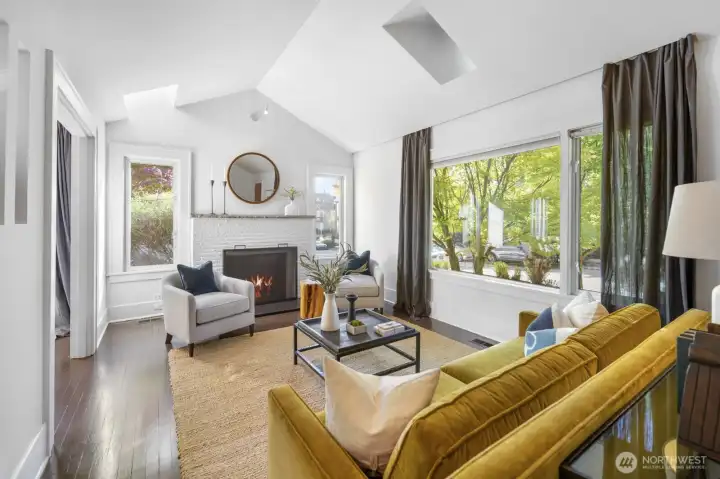 Large picture window frames greenery; vaulted ceiling and skylight amplify natural light throughout.