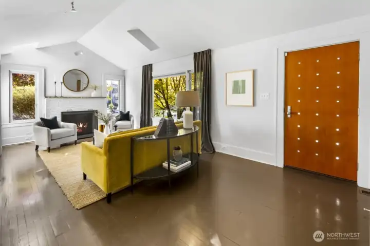 Statement front door opens to an a=spacious living room with hearth, tall ceilings, and garden views.