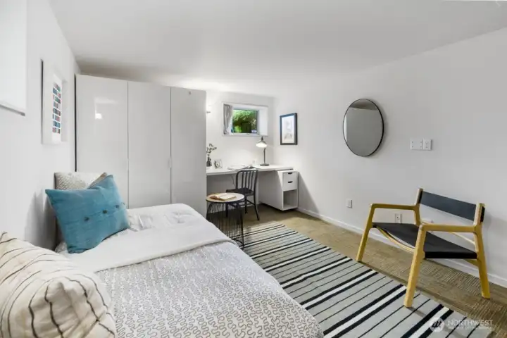 Bright lower-level bedroom/office with wardrobe storage, desk niche, and daylight window.