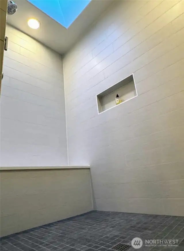 Shower surround in guest bath with niche, bench, and skylight.