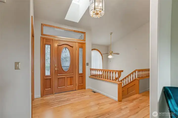 Step into a warm and welcoming foyer filled with natural light from a skylight above, highlighting true oak hardwood floors and elegant millwork.