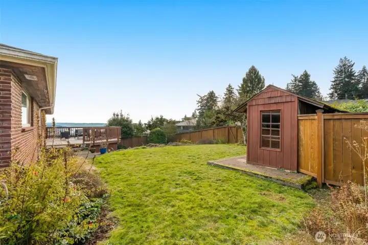 Grassy fenced backyard for play, separate lower patio area, potting shed