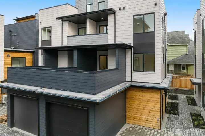 The back exterior shows off the layered design with wood accents, a balcony, and an attached garage.