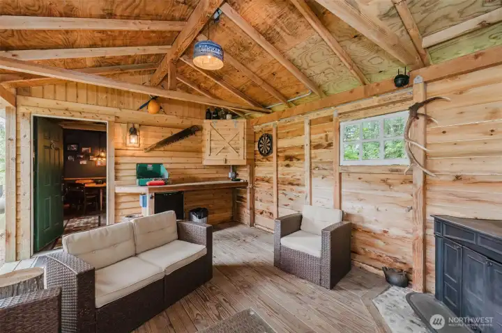 Attached to the saloon is a relaxed cabana designed for year-round enjoyment. A wood-burning stove keeps the space comfortable, while the rough-hewn bar top, comfortable seating area, and partially open-air design invite guests to linger. Attached to the saloon is a relaxed cabana designed for year-round enjoyment. A wood-burning stove keeps the space comfortable, while the rough-hewn bar top, comfortable seating area, and partially open-air design invite guests to linger.