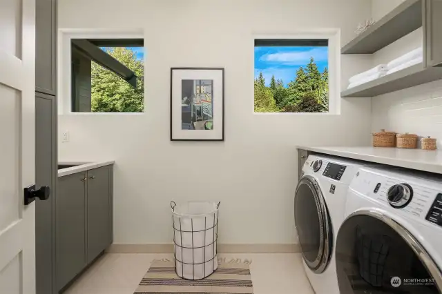 Upper level laundry has washer and dryer, floating shelves, cabinet storage and laundry sink.