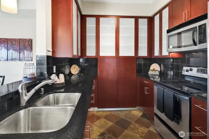 This elegant space features rich cherry cabinets, sleek black granite, and a softly illuminated tile backsplash.