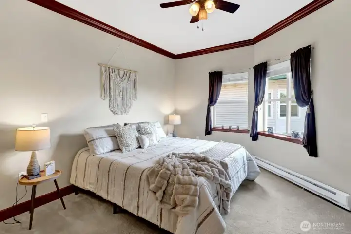 Generous primary suite offering panoramic southwest-facing windows and a peaceful atmosphere. Note the cherry crown molding and ceiling fan.