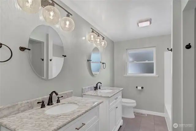 Fully remodeled bathroom with dual sinks and sleek modern lighting.