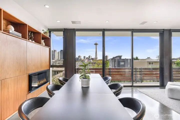 The elevated open-concept living space opens wide with sliding glass walls, dissolving boundaries to reveal breathtaking views of the Space Needle, Elliott Bay, and the city beyond.