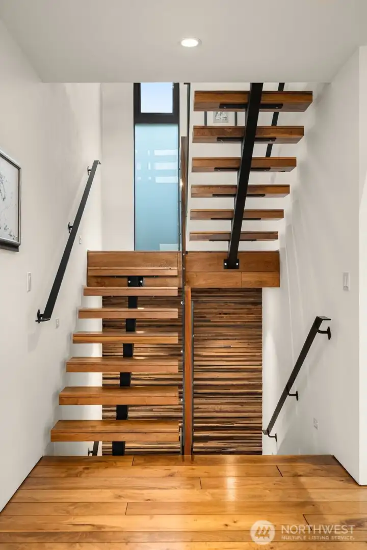 Floating stairs, framed in light, become a gallery-like centerpiece — each step a rhythm of wood and steel leading you upward into living spaces that breathe.