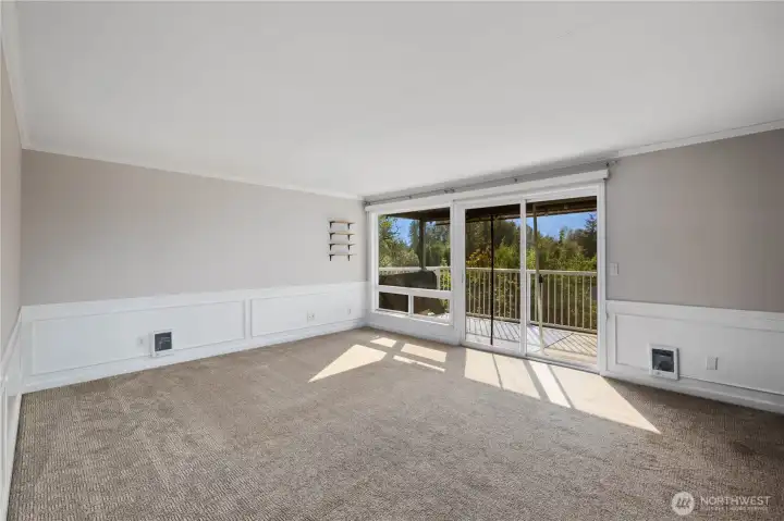 Living Room: Light-filled living room with large windows and sliding glass doors that open to the covered balcony. Neutral finishes, crown molding, and treetop views create a comfortable, inviting retreat.