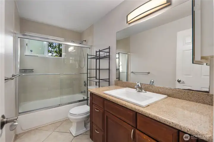 Bathroom: Full bathroom with granite vanity, modern lighting, and tile surround tub/shower combo. Ample counter space and storage blend convenience with clean, timeless design.