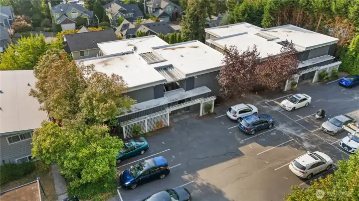 Community Exterior (Aerial): Aerial view of the Kirklandaire Condominiums, surrounded by lush greenery and nestled in a quiet residential setting. Ample surface parking and well-maintained buildings create a welcoming community just minutes from downtown Kirkland.