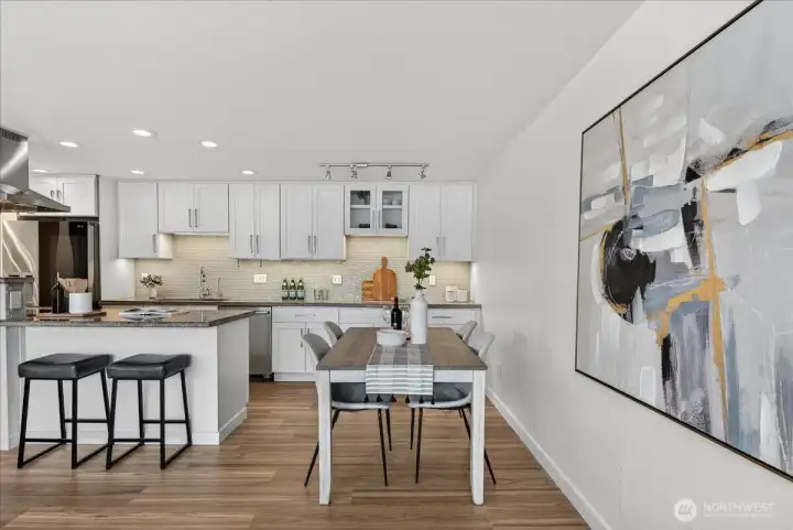 The open dining area sits perfectly next to the chef's kitchen and living space, creating an effortless flow for everyday meals and entertaining alike. Warm new LVP floors, under-cabinet lighting, and the crisp white cabinetry with mosaic tile backsplash set an elevated yet welcoming tone — while the generous dining space easily accommodates a full table.