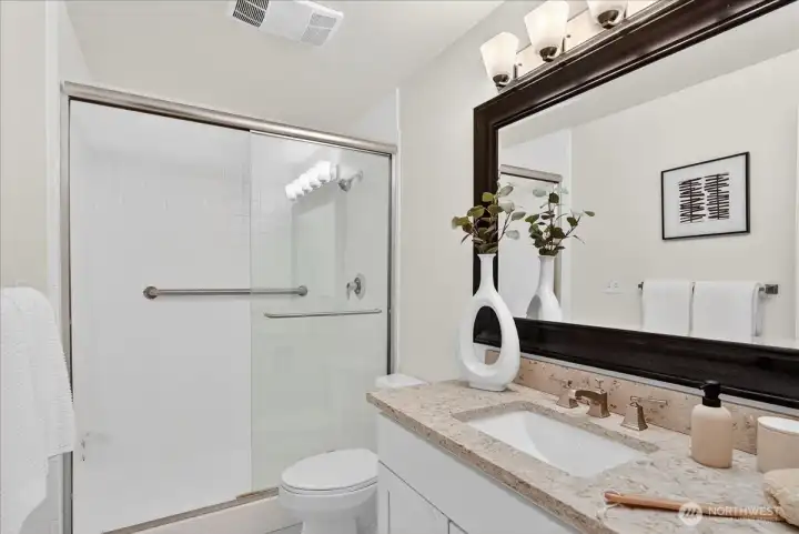 The primary three-quarter bath features a granite vanity countertop, undermount sink with brushed nickel fixtures, a large framed mirror, white cabinetry, and a glass sliding door shower — clean, bright, and thoughtfully finished throughout.