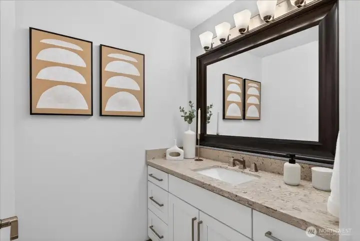 A beautifully appointed full bathroom featuring granite counters, undermount sink, brushed nickel fixtures, white cabinetry, and a generously sized framed mirror — bright, clean, and move-in ready.