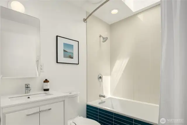 The main floor bath (one of two in the main house) boasts an overhead skylight and tiled surround as well as a large vanity cabinet.