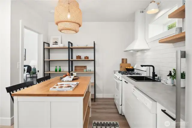 The island features butcher block counters with open storage underneath that adds a nice warmth to the quartz counters on the right.