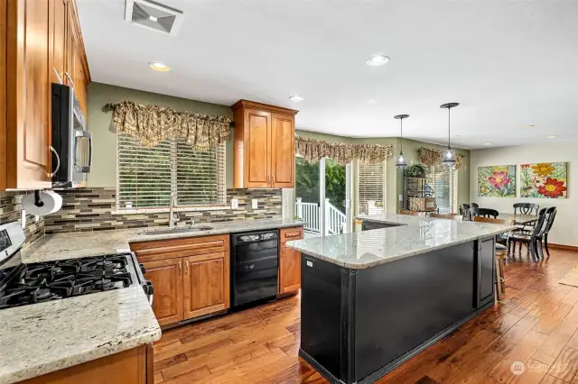 Granite countertops and cherry laminate wood flooring throughout kitchen and living space.