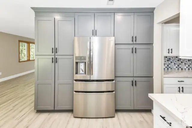View of cabinets and refrigerator with a peak into living room.