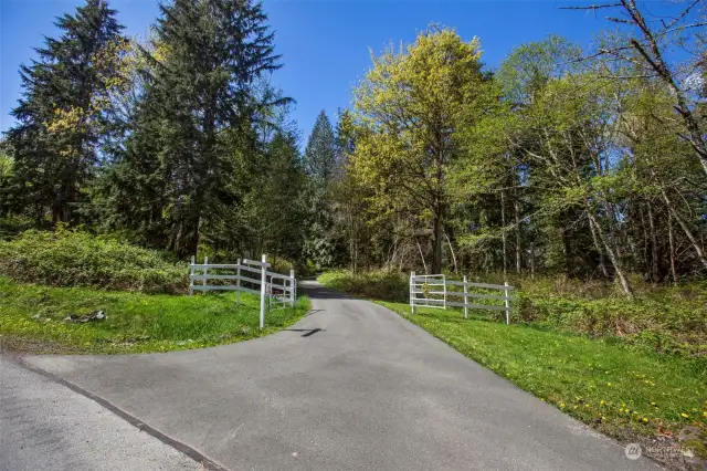 Extended paved driveway through the trees with entry gate