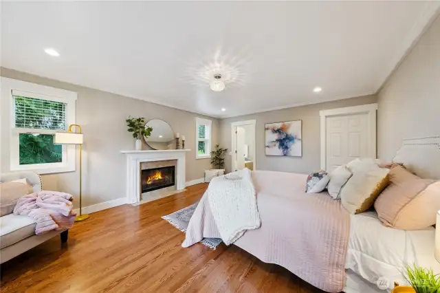 Spacious primary suite with oak floors, wood-burning fireplace, crown molding, large walk-in closet.