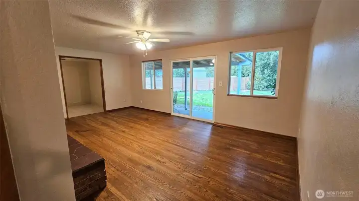 View from the hallway to the family room with hardwood floors, slider to the backyard, ceiling fan, and brick fireplace.