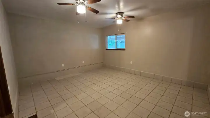 A large extra finished room with tile flooring and two ceiling fans. This room is conveniently off of the family room, has its own exterior entrance door, and is ready for multi-purpose use.