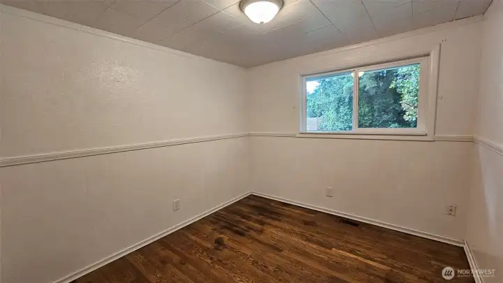 Bedroom number three with hardwood floors, a window to the backyard, closet, and bright walls.