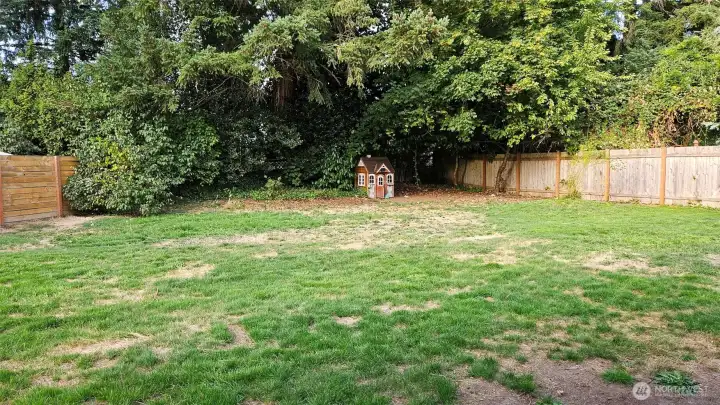 Large, fenced backyard with some trees and easy-maintenance landscaping.