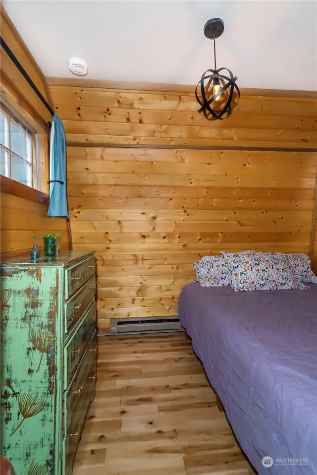 main level bedroom with pine flooring and paneling is warm and cozy.