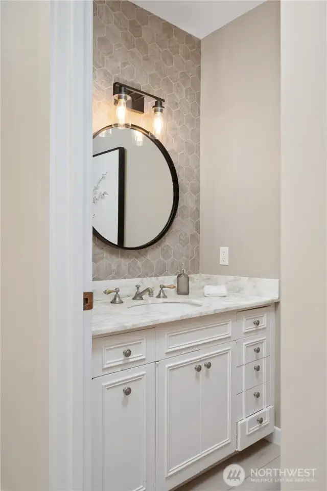 Main level powder room features antique cabinetry, marble counter top, pewter faucet, and hexagon accent tile.