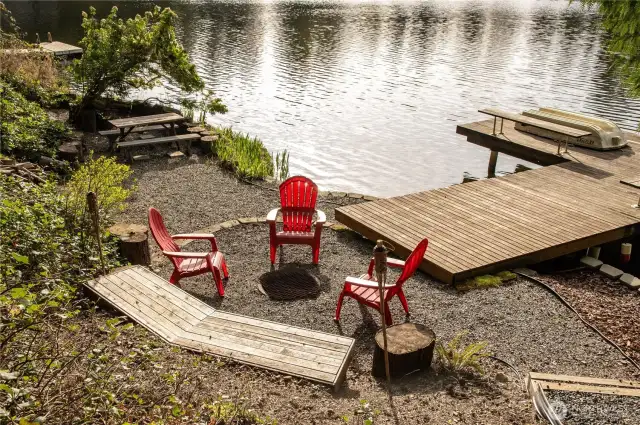 Lakeside recreation area with fire pit, built in seating, picnic area, and dock.