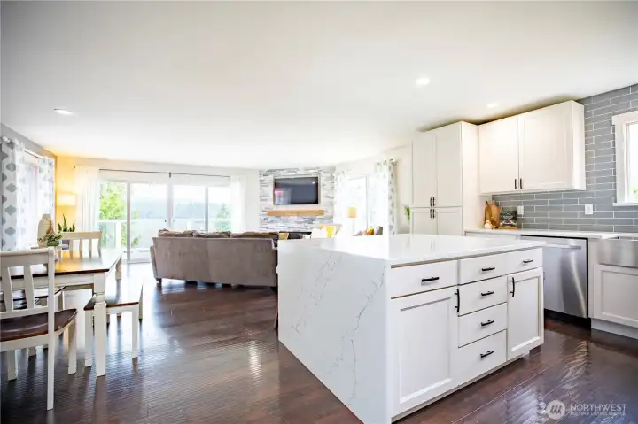 The great room includes the kitchen, living room, and dining room with double sliders on the deck with a view of the lake and the Olympic Mountains.
